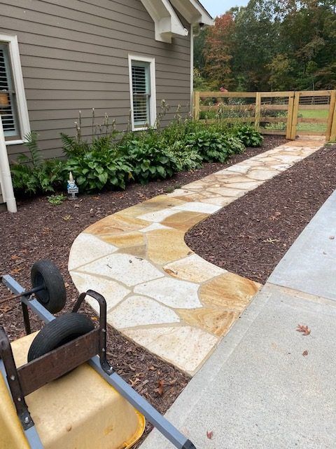 Backyard stone walkway beside a house, with a gravel border and garden bed.