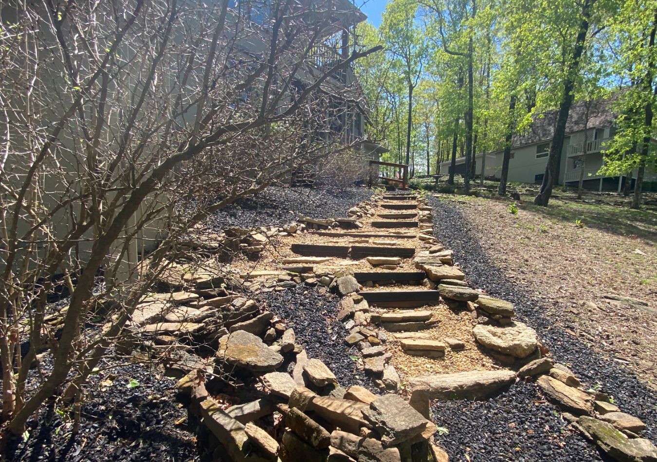 Stone steps climbing a wooded hillside beside a rocky path in bright sunlight