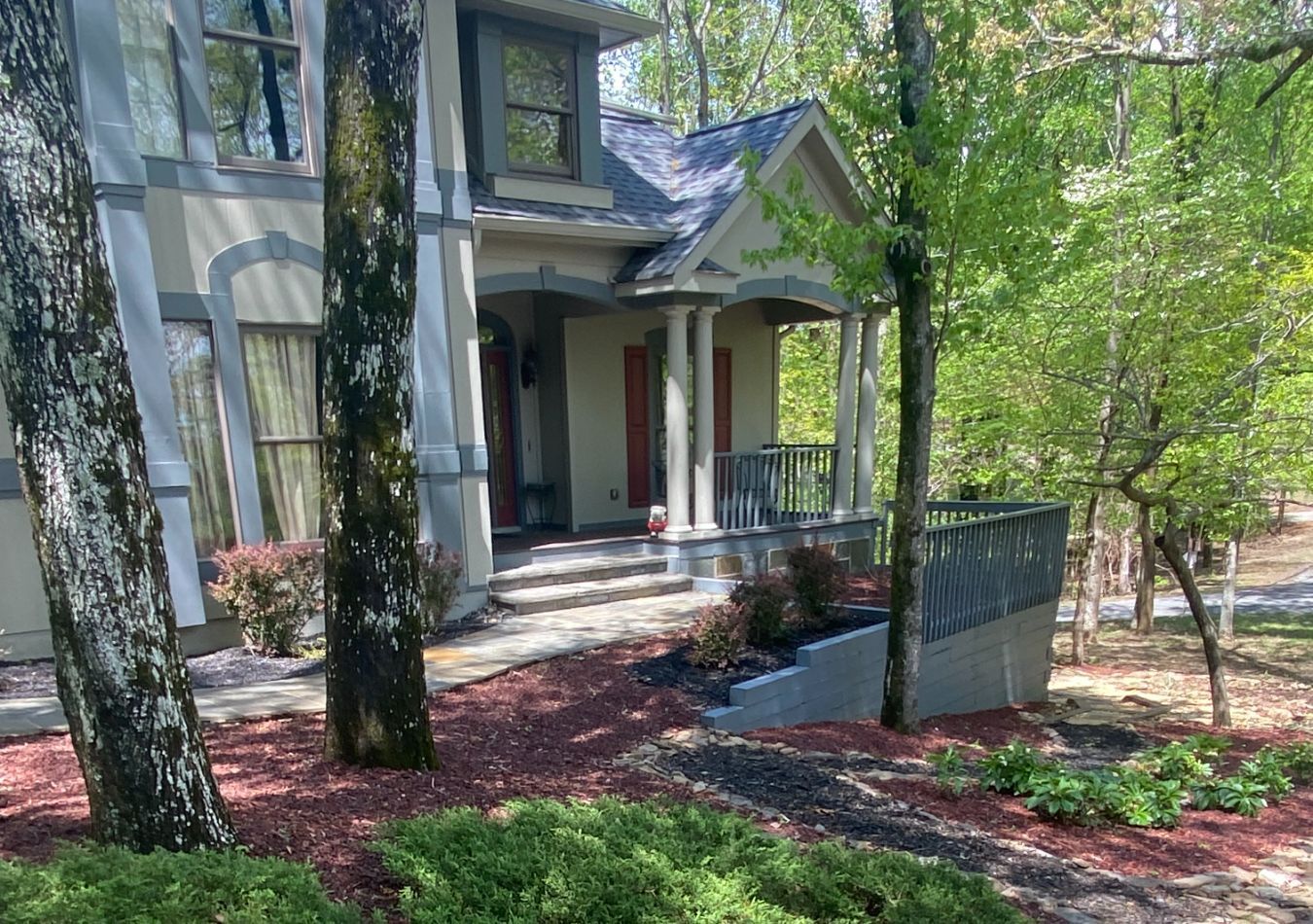 Front porch of a house with white columns, red door, and a ramp beside trees and landscaping