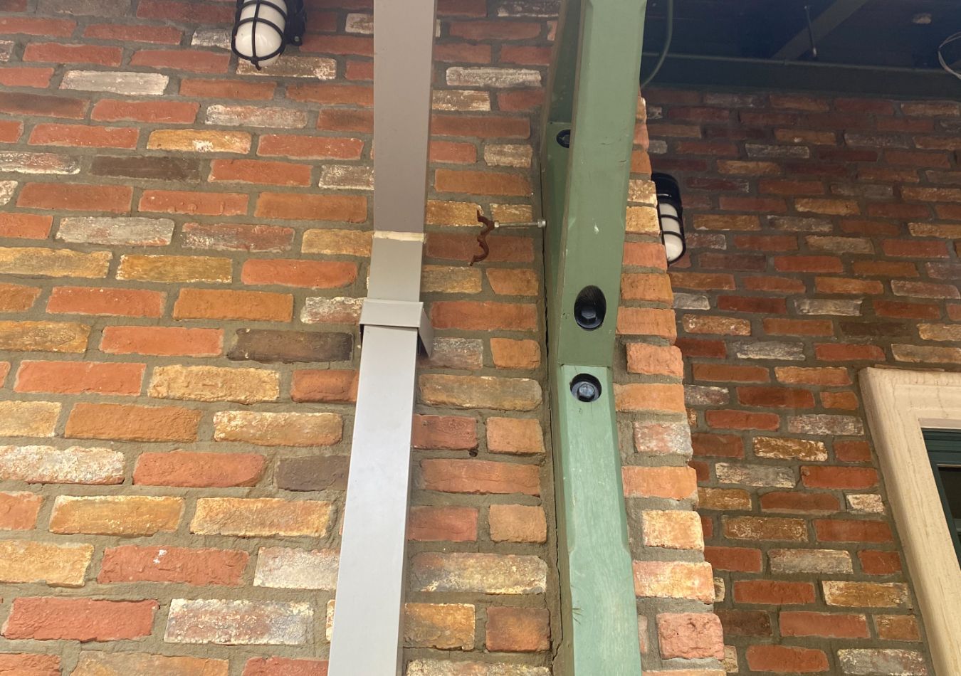 Brick building wall with two vertical metal downspouts and wall-mounted lights near a window