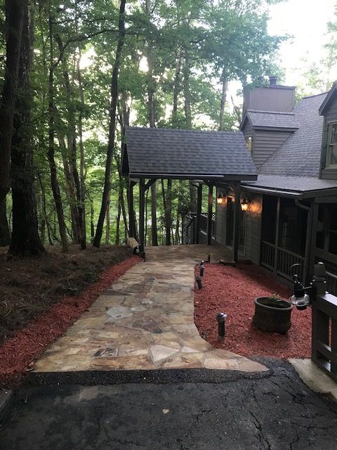 Stone walkway to a dark house in a wooded yard, with red mulch and trees along the path