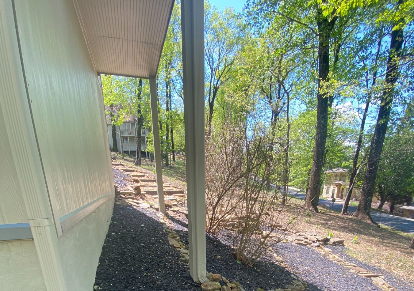 Side of a beige building beside a wooded gravel path on a sunny day