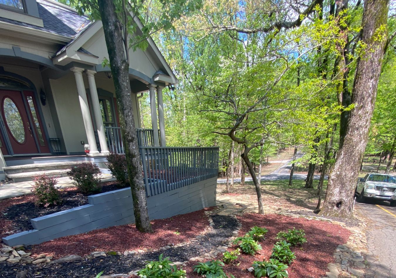 Front porch of a house with stone steps, railing, and trees in a landscaped yard