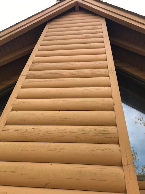 Gray louvered window shutters on a beige wall, closed and secured with metal hinges.