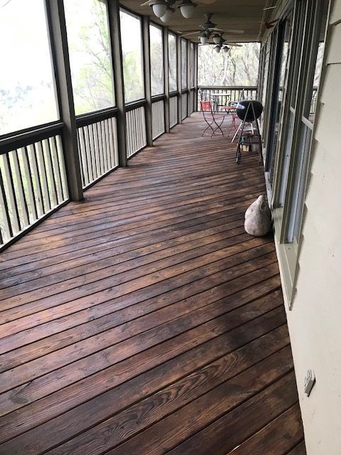 Covered wooden porch with wet planks, railing, a chair, and a bag by the wall