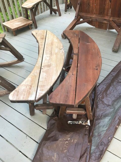 Curved wooden benches on a deck, one light and one dark, beside other rustic furniture.