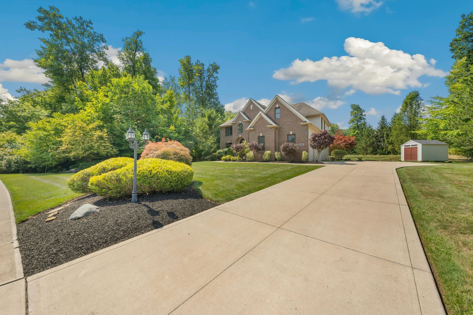 Suburban house with curved driveway, landscaped lawn, and blue sky with clouds