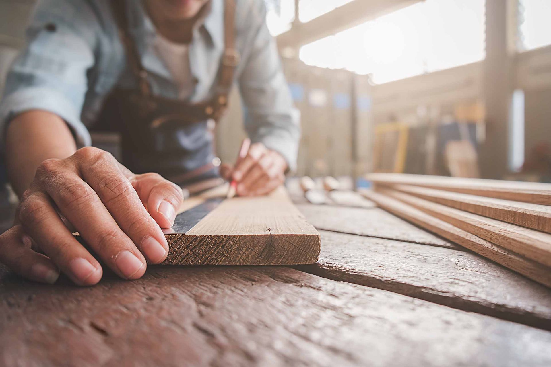 Person sanding a wooden plank on a workbench in a sunlit workshop