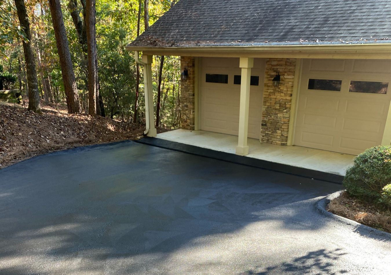 Driveway leading to a tan garage with two doors, surrounded by trees and woods.