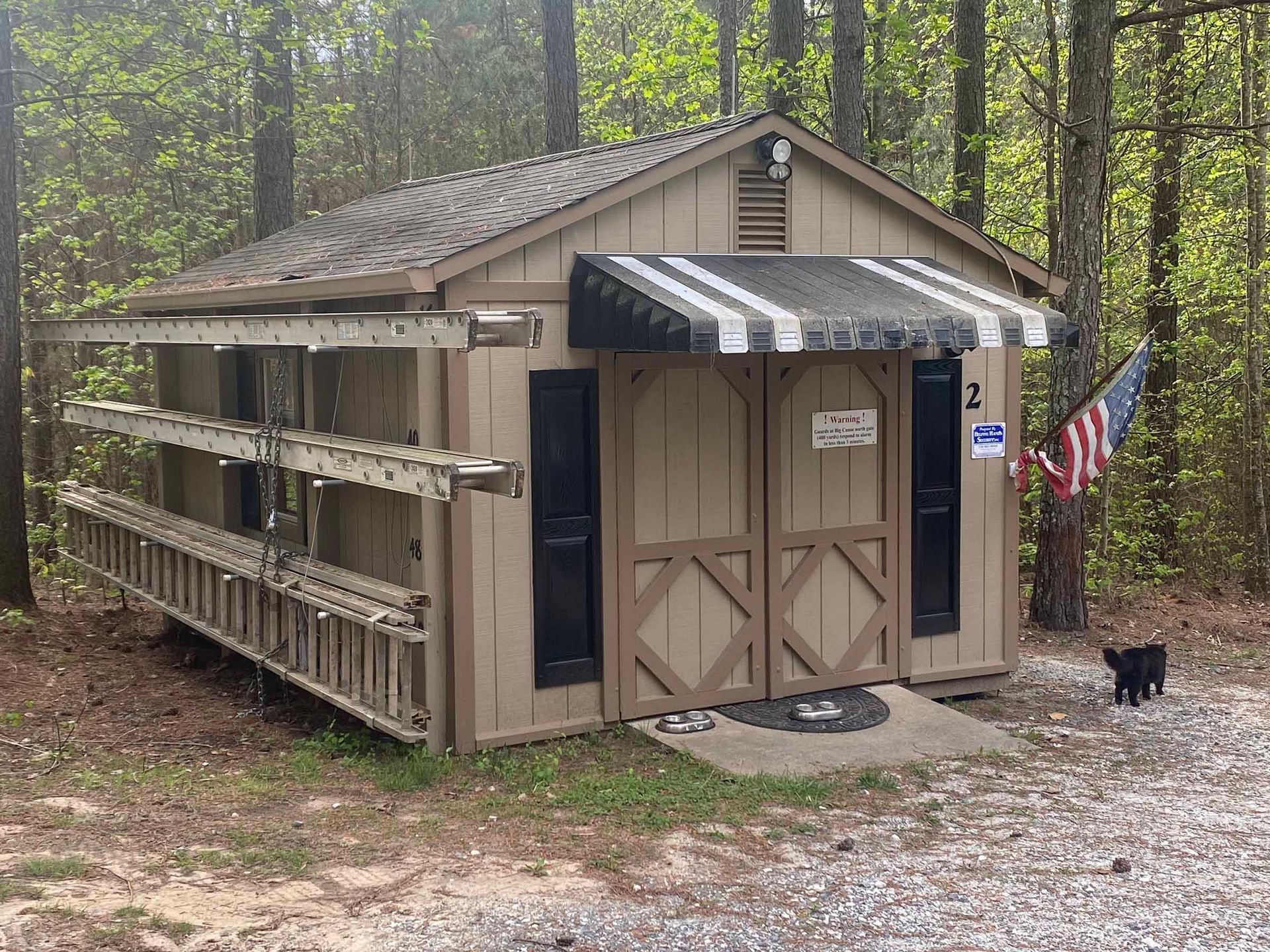 Small tan shed with ramps and awning in a wooded campground setting