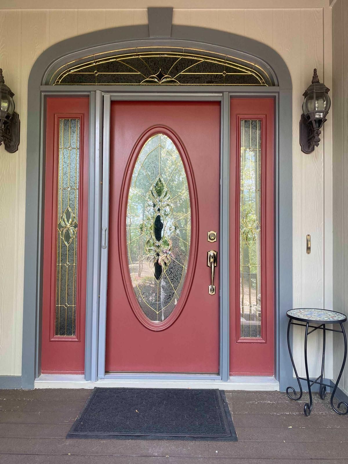 Red front door with oval glass panel, sidelights, and black lanterns on a covered entryway