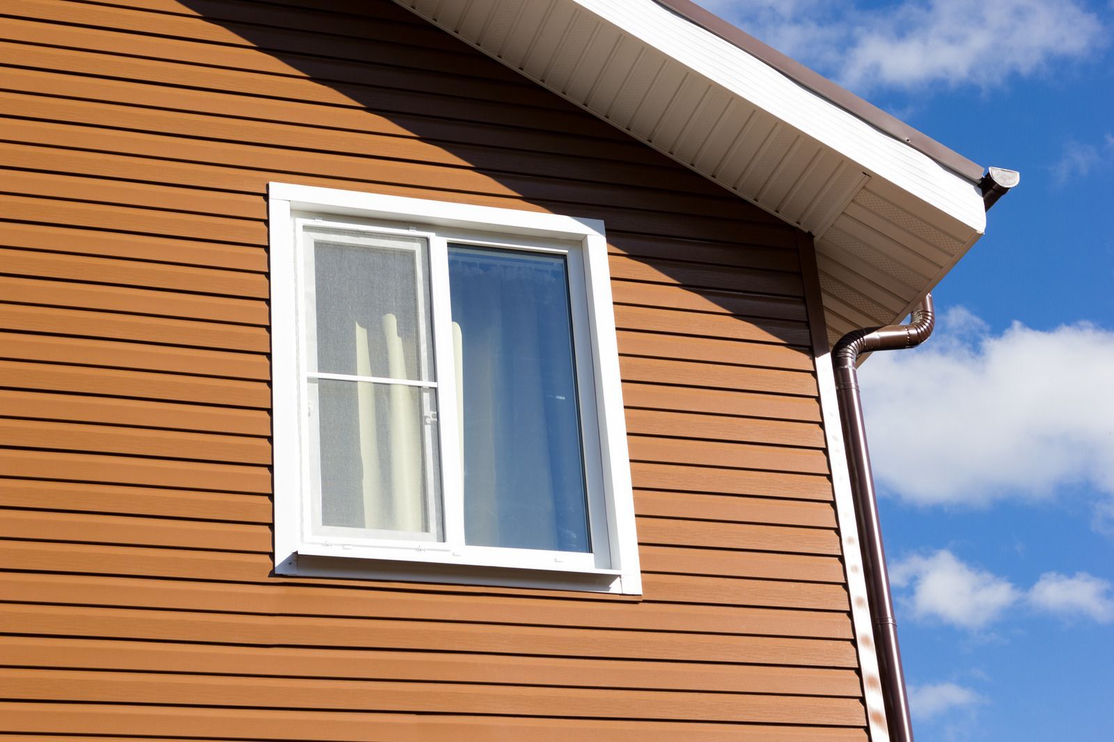 White-framed window on a brown wooden house under a blue sky