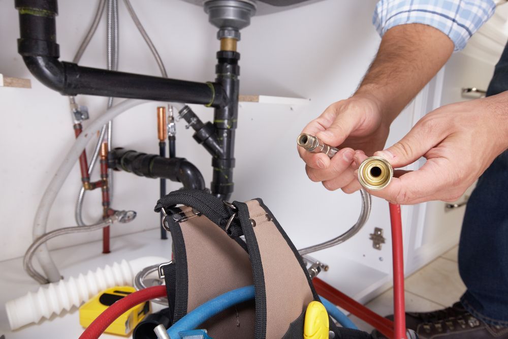 A Plumber is Fixing a Pipe Under a Sink — JMJ Plumbing and Electrical NSW In Tumbi Umbi, NSW