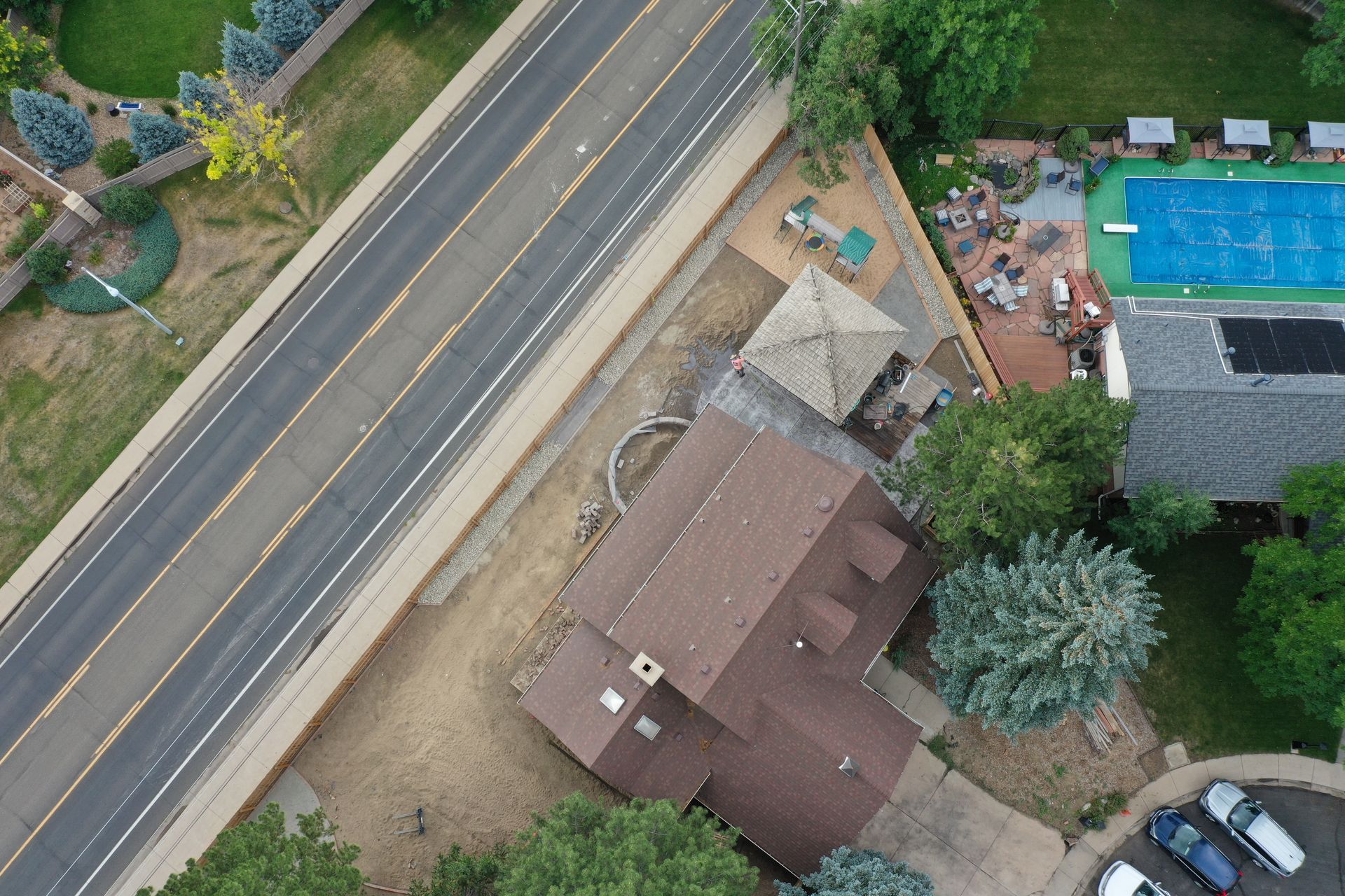 Aerial view of a house with a brown roof, next to a road, and a pool.