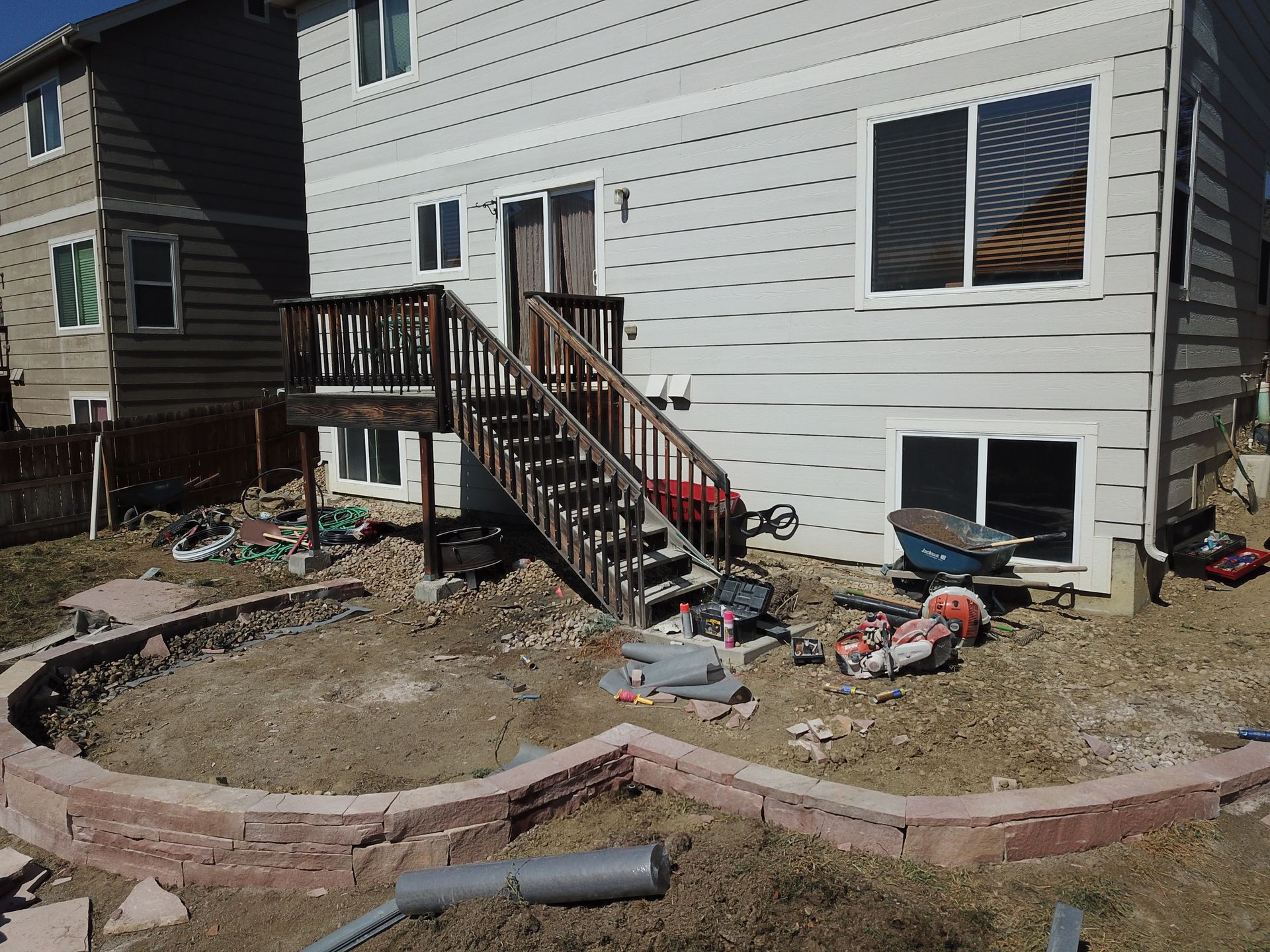 Backyard with a raised deck, retaining wall, and construction materials scattered around.