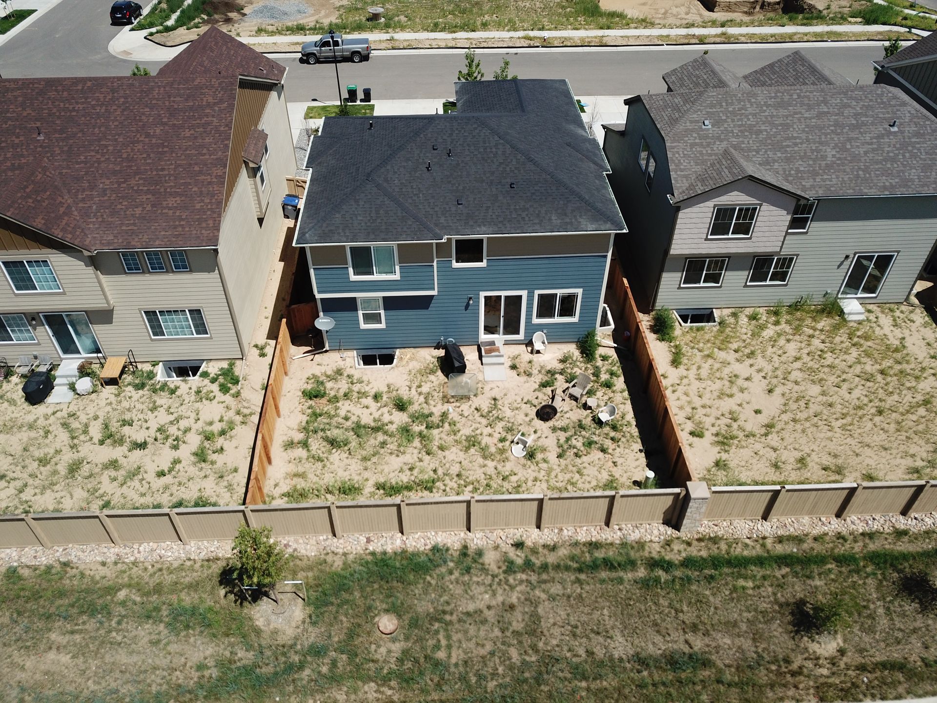 Aerial view of three houses, a blue one in the center with a dark roof and a brown one on either side.