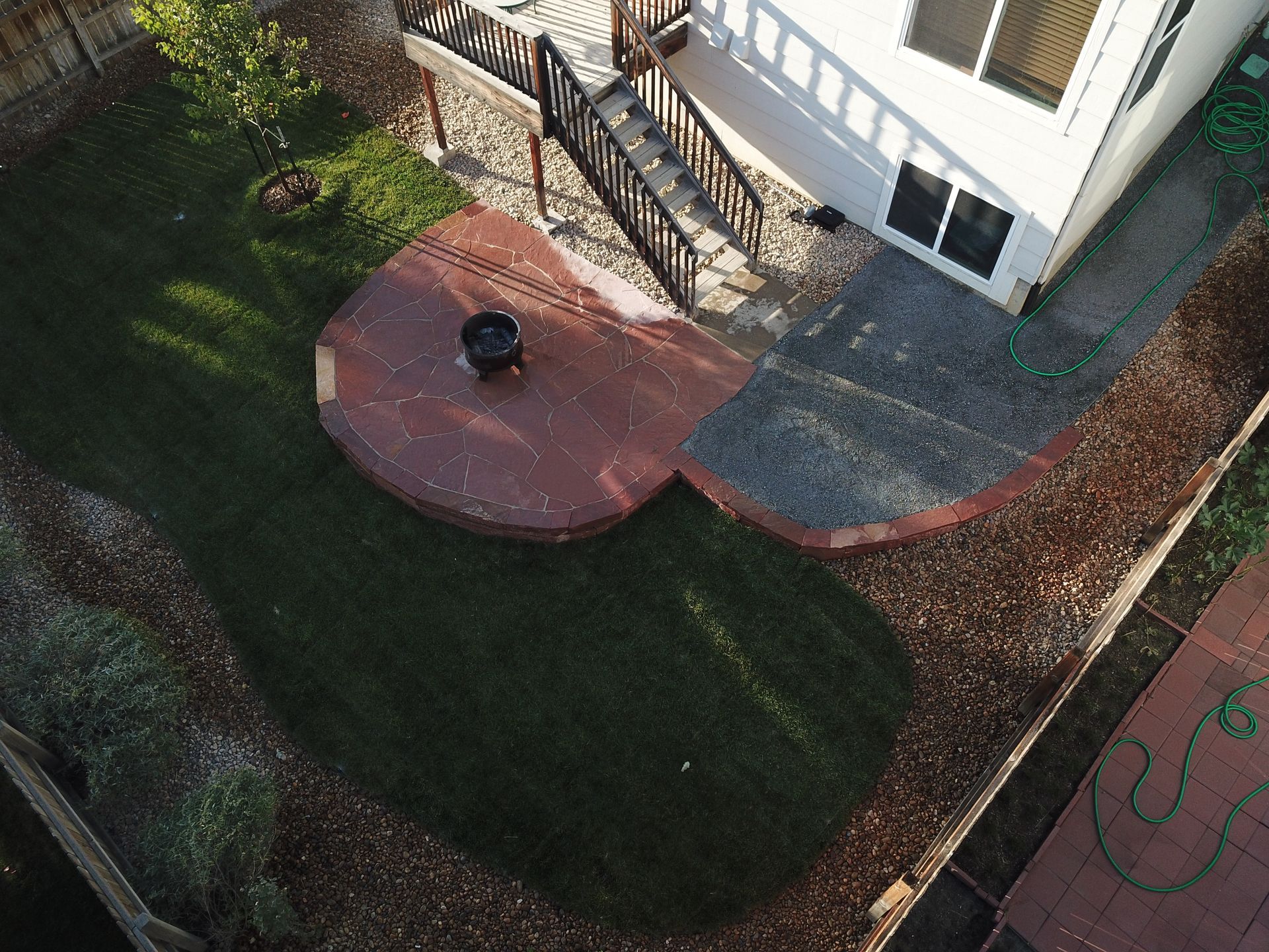 Aerial view of a backyard with a fire pit, patio, green lawn, and house.