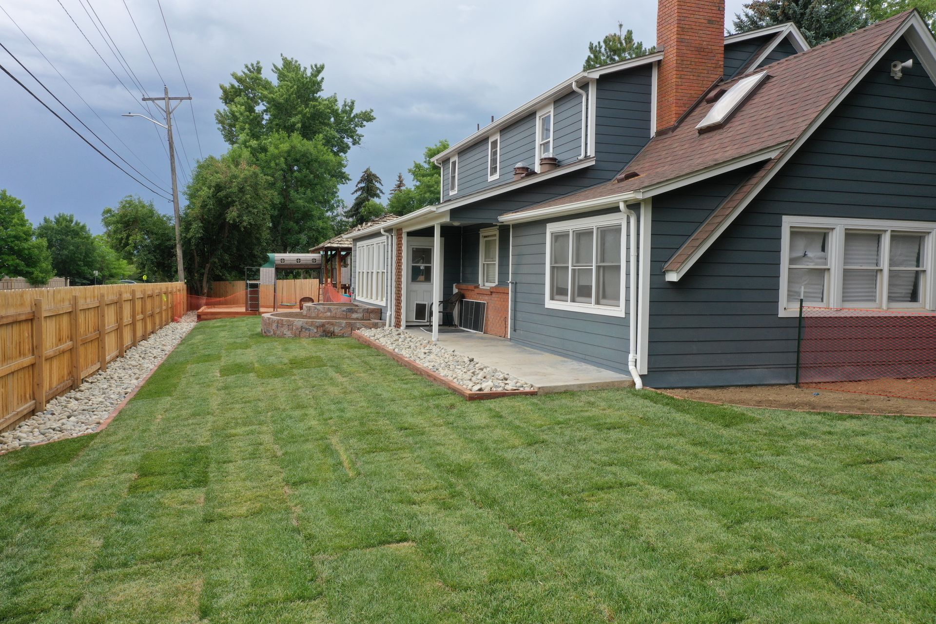 Backyard view of a house with green lawn, wooden fence, and patio.
