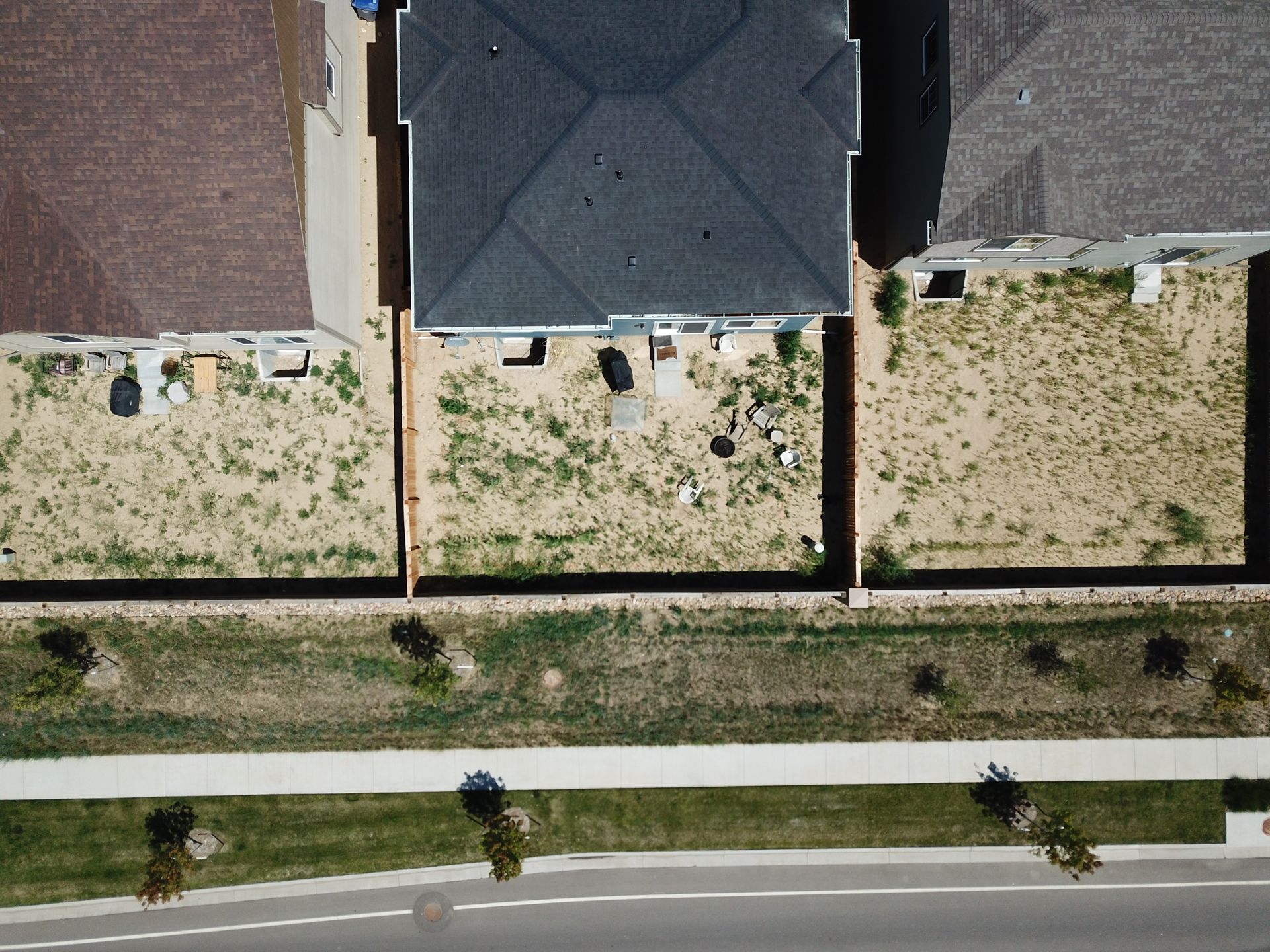Aerial view of three houses with brown yards, a street, and a sidewalk.