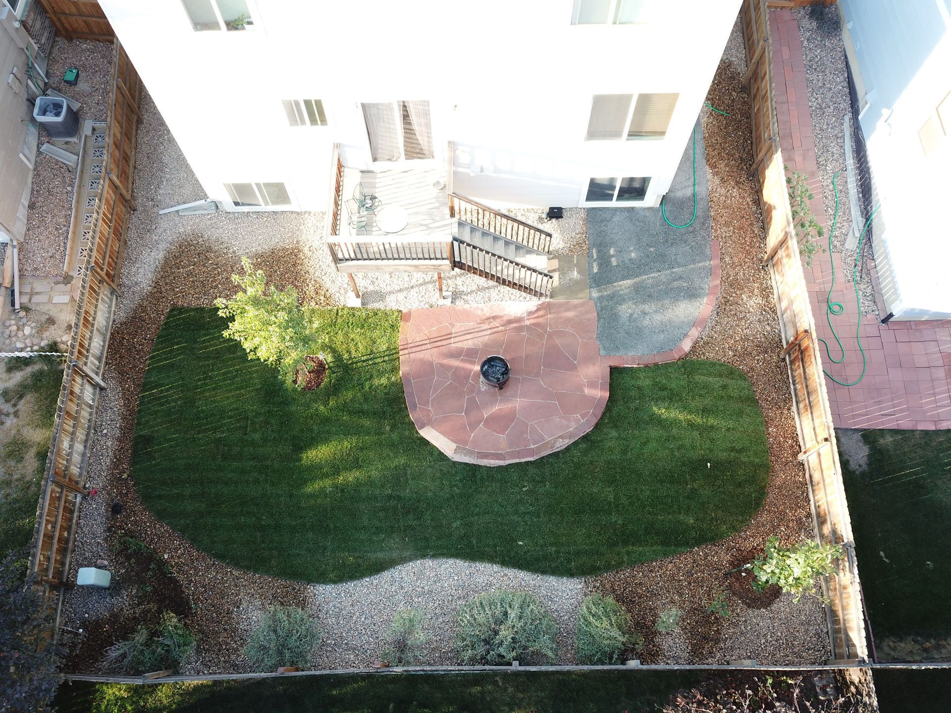 Aerial view of a backyard with a circular fire pit, lawn, landscaping, and a house.