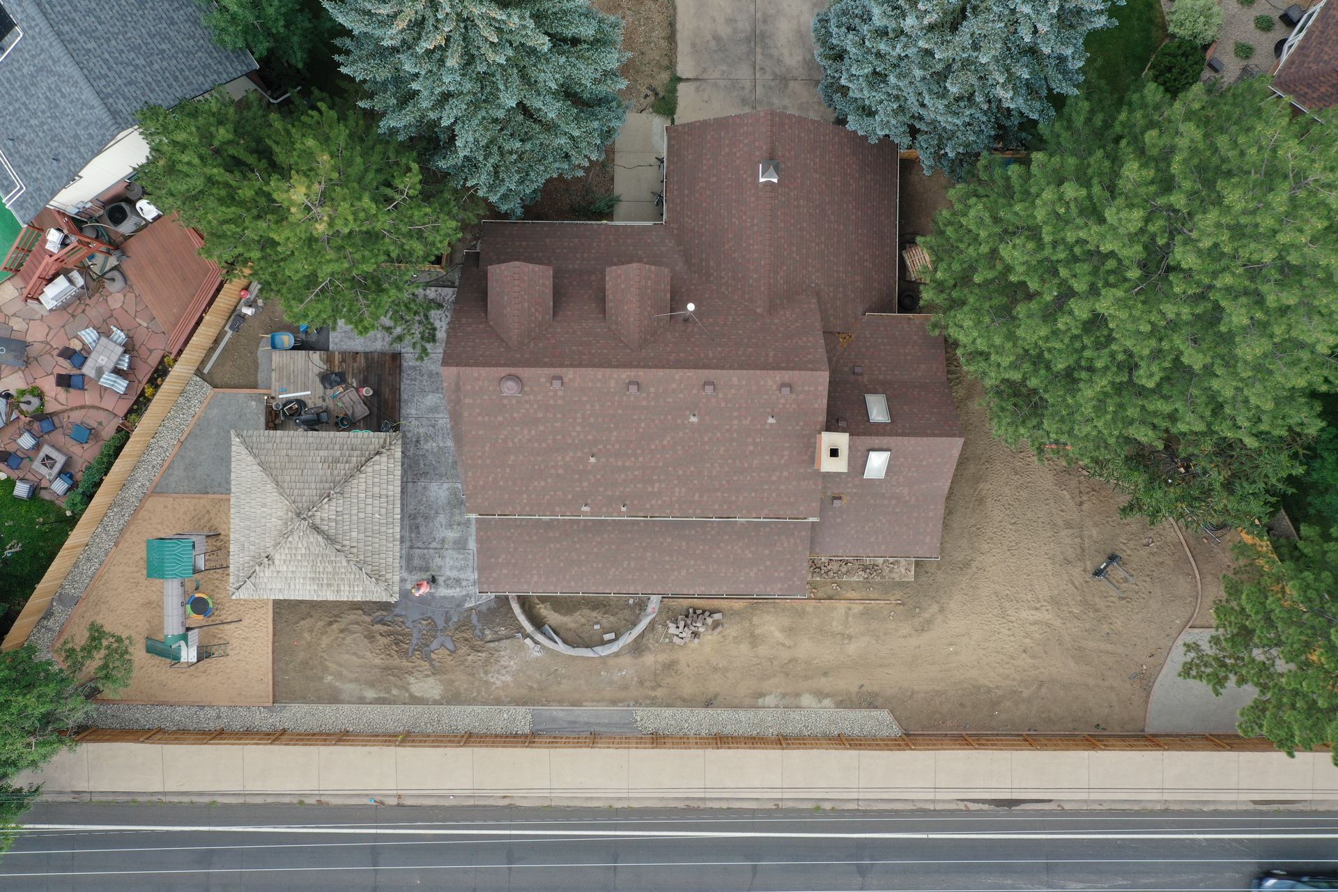 Overhead view of a house with a brown roof, surrounded by trees and a stone patio.