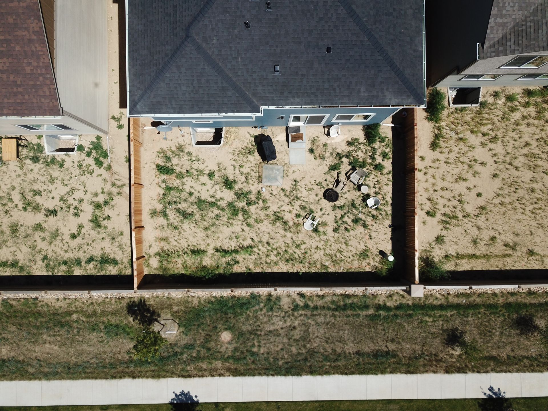 Overhead view of three houses, a sidewalk, and a strip of grass. Dry grass yards, brown fences.