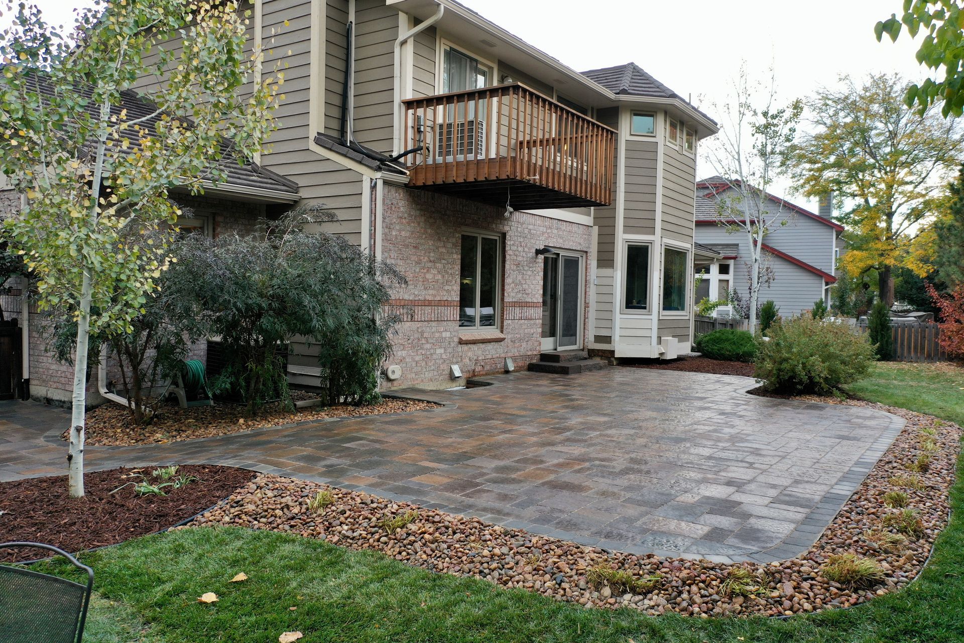 Backyard patio with brick house, balcony, and landscaping with brown mulch and green grass.