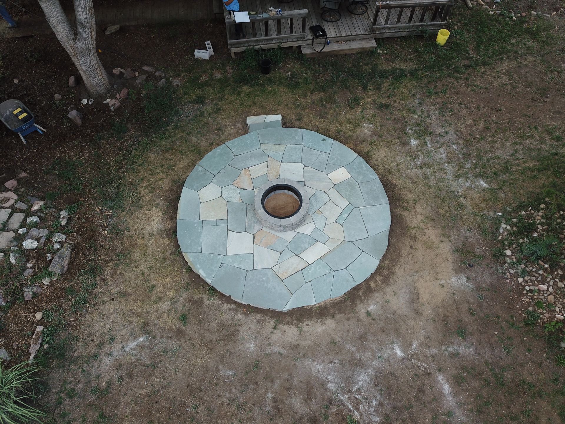 Overhead view of a circular stone patio with a central hole, surrounded by grass and a house in the background.