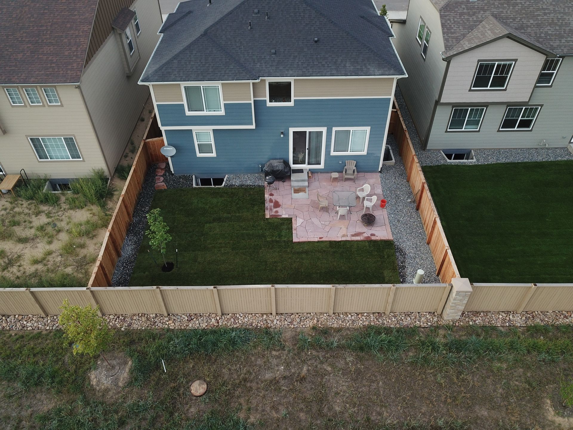 Backyard view of a two-story blue house with a patio, lawn, and wooden fence.