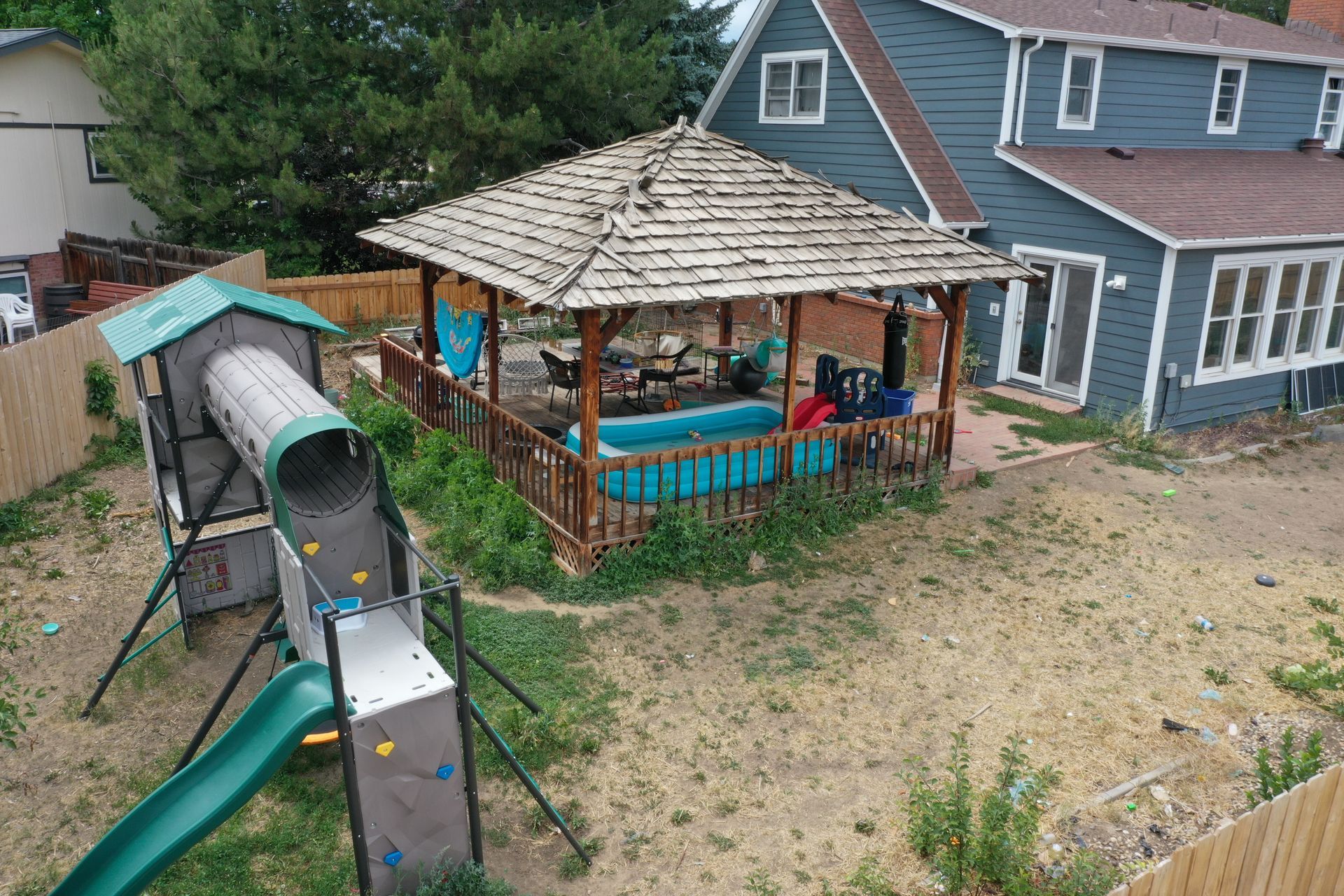 Backyard with a gazebo and play structure near a blue house.