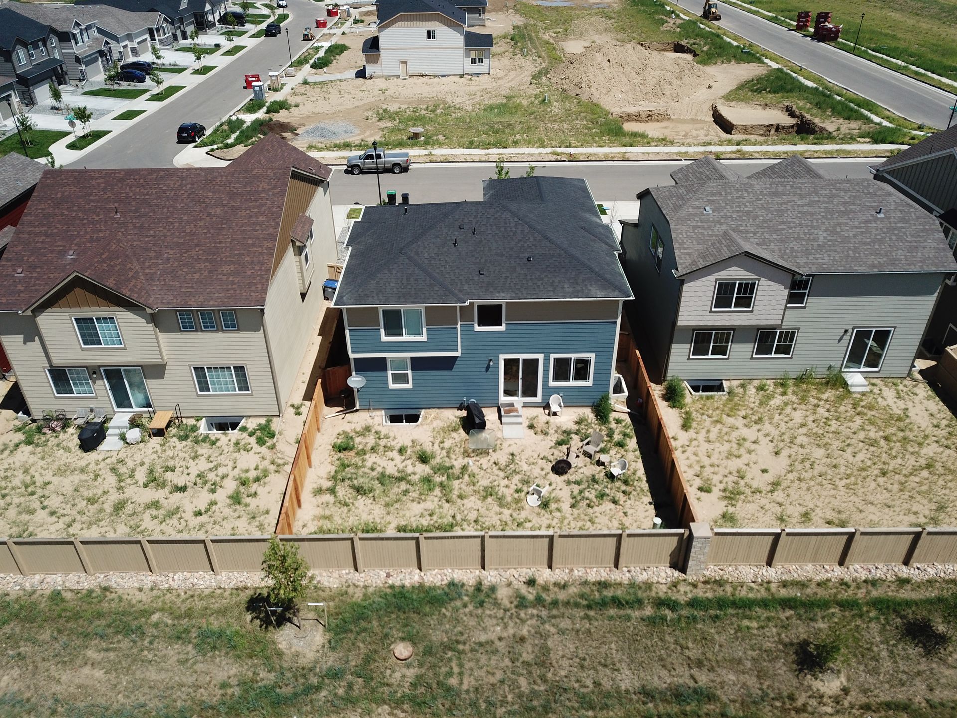 Aerial view of three houses, tan fence surrounds brown/dry yards, blue and brown houses with dark roofs.