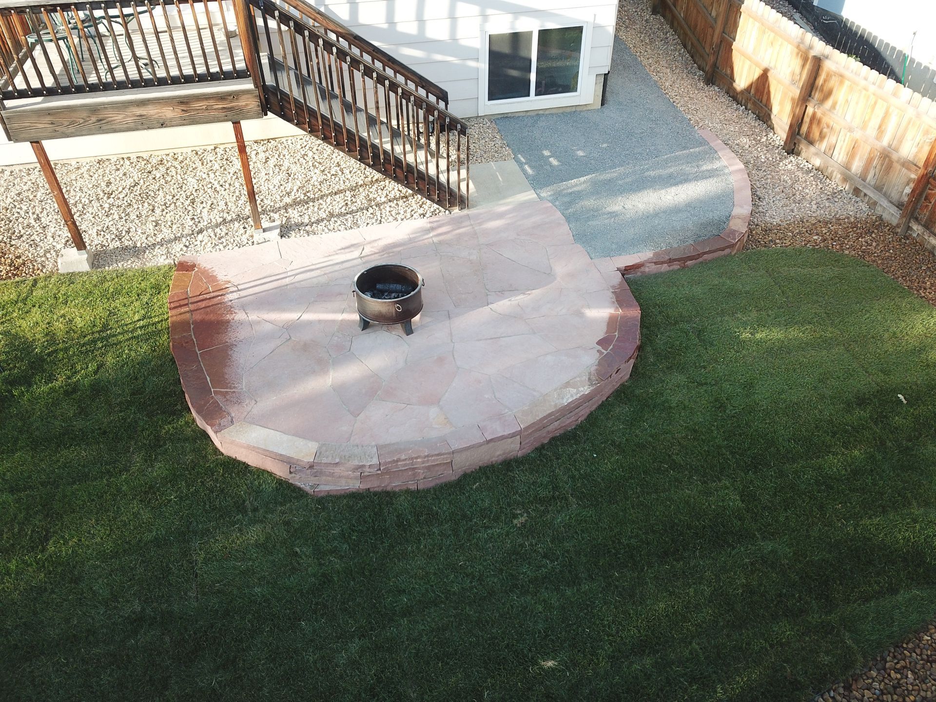 Backyard with a stone patio, fire pit, stairs, deck, and green lawn.