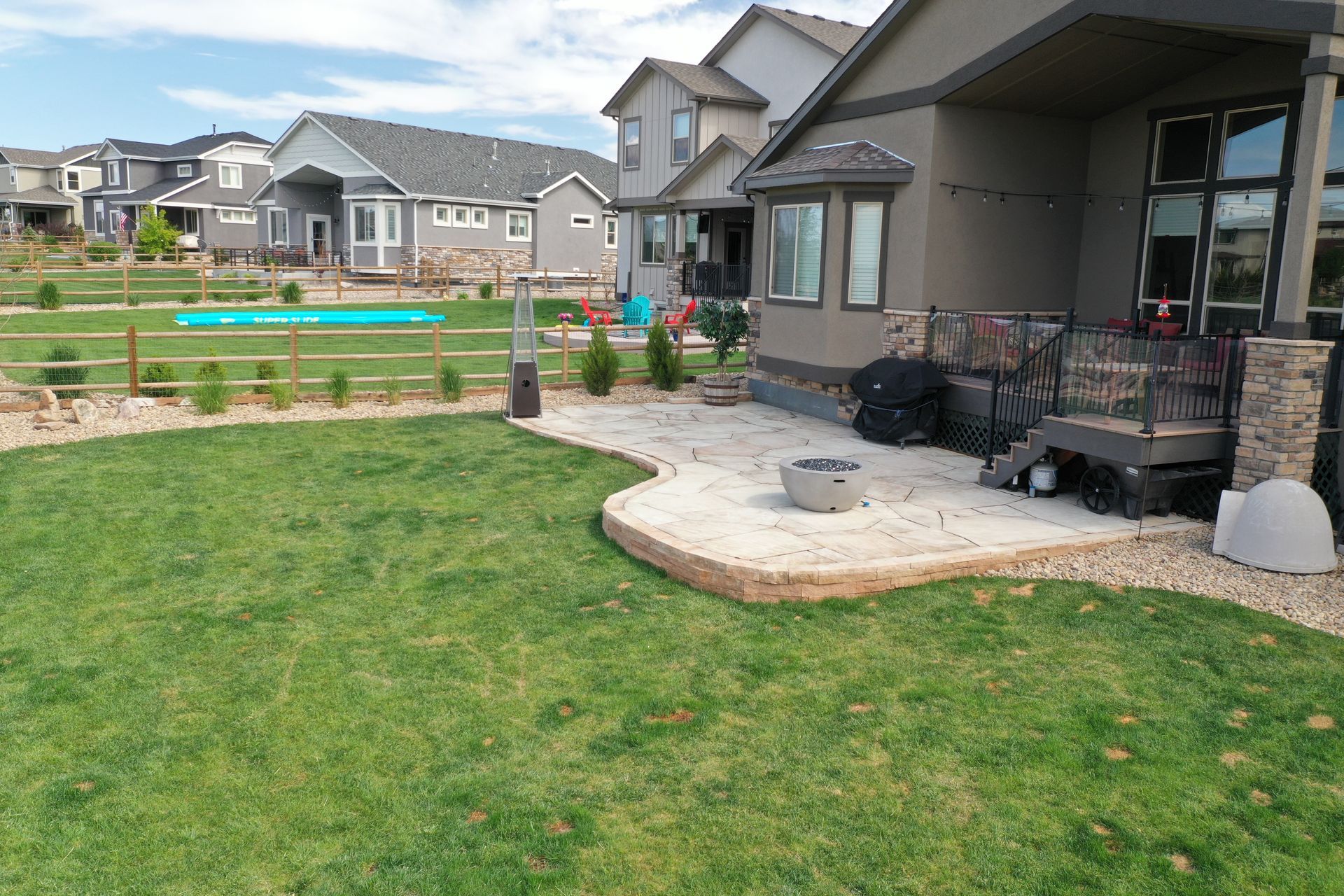 Lawn with stone patio and fire pit next to a house with other houses in the background.