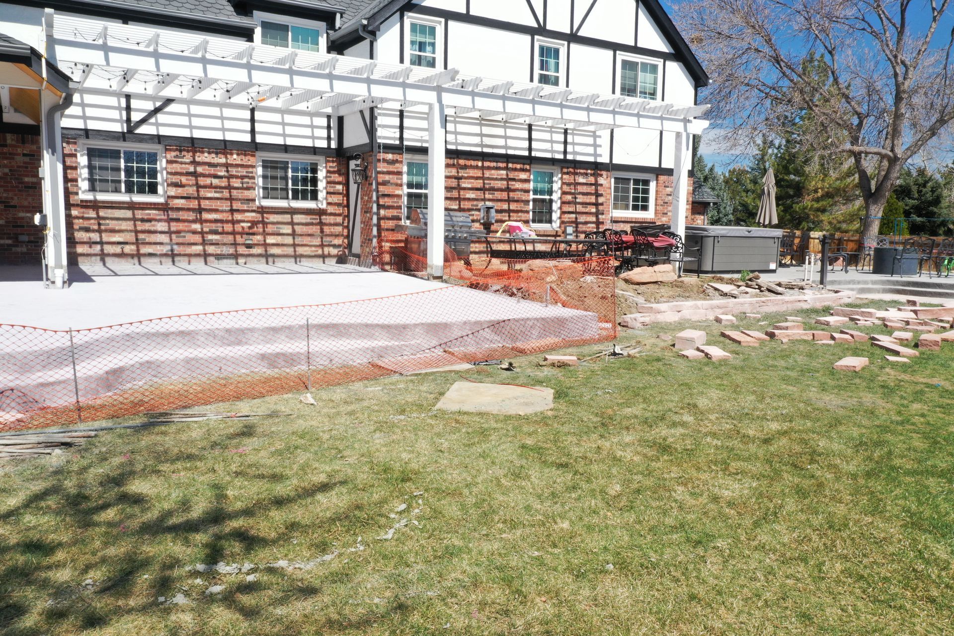 Backyard with red brick house under construction, pergola, grass, and safety fencing.