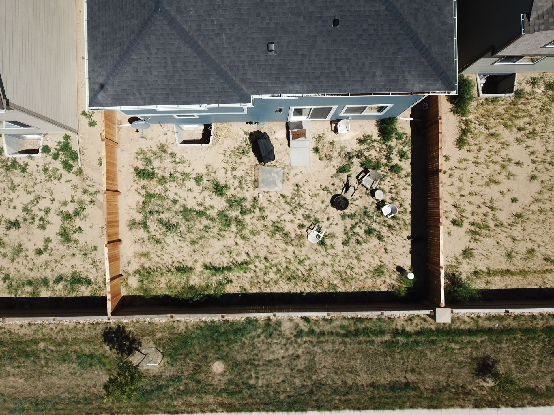 Aerial view of a blue house with a yard. Brown fences border the yard with sparse grass.