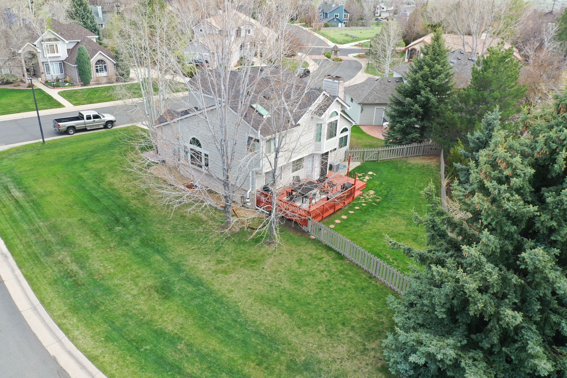 Aerial view of a gray house with a red deck and green lawn. A white fence borders the yard.