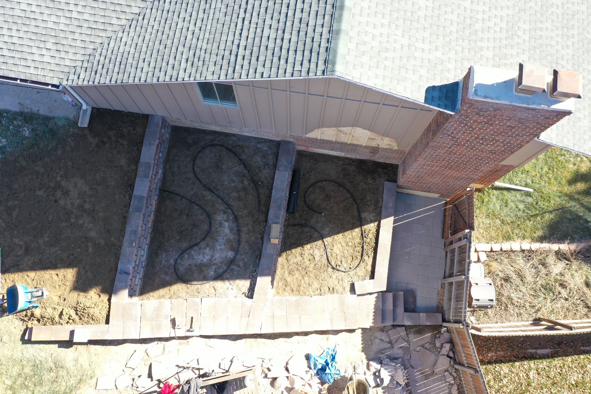 Overhead view of a backyard with a brick patio, grass area, and a dark, curved design in the grass.