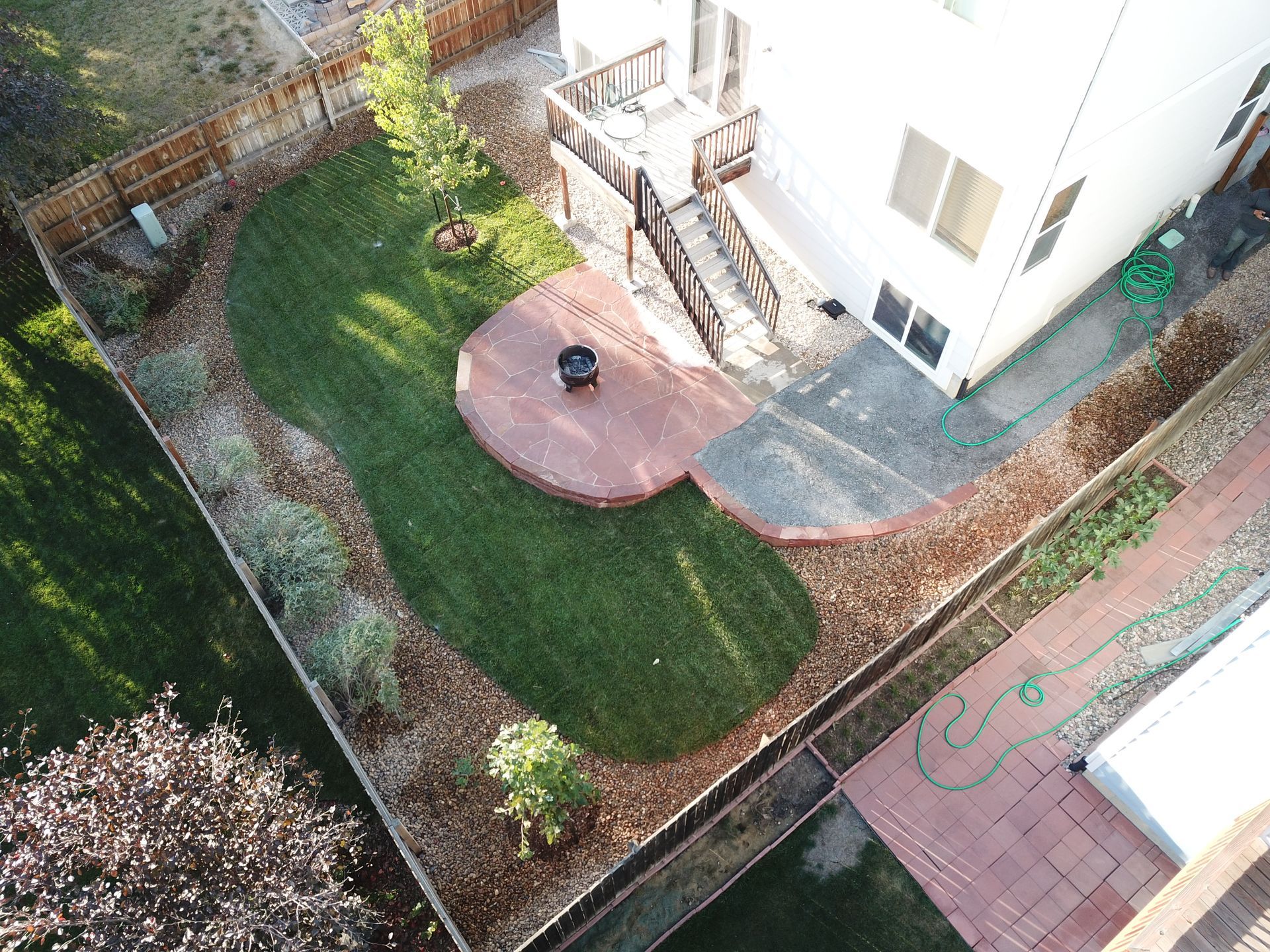 Overhead view of backyard with a deck, patio, green lawn, and rock-lined landscaping.