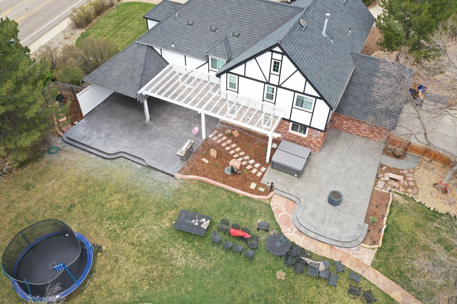 Overhead view of a two-story house with a patio, pergola, trampoline, and lawn. Black and white exterior.