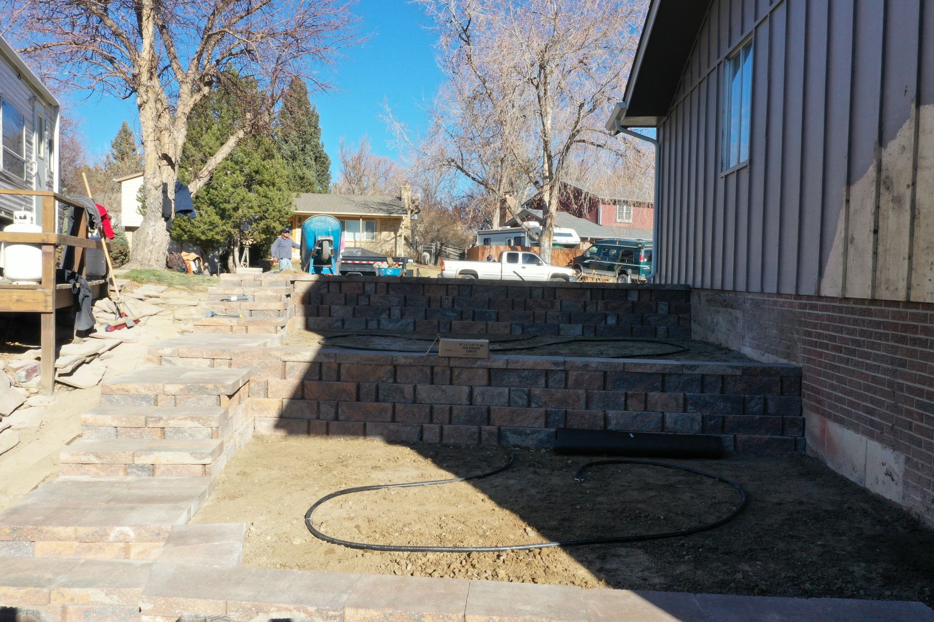 Brick retaining wall with stairs leading to a backyard, with a house on the right, and trees in background.
