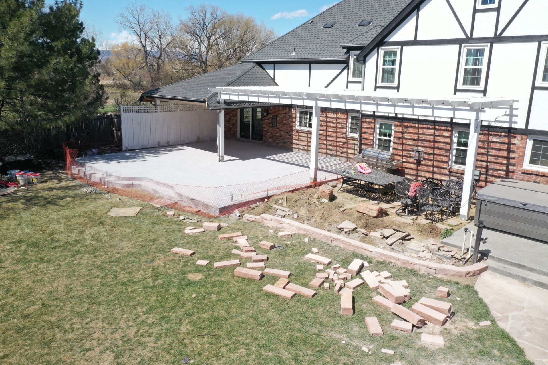 Backyard with unfinished patio construction; bricks scattered on grass. Tudor-style house visible.