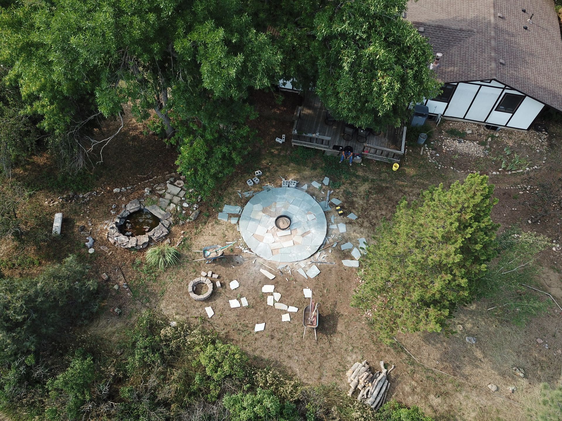 Overhead view of a grassy clearing with a circular structure, fire pits, and a thatch-roofed building.