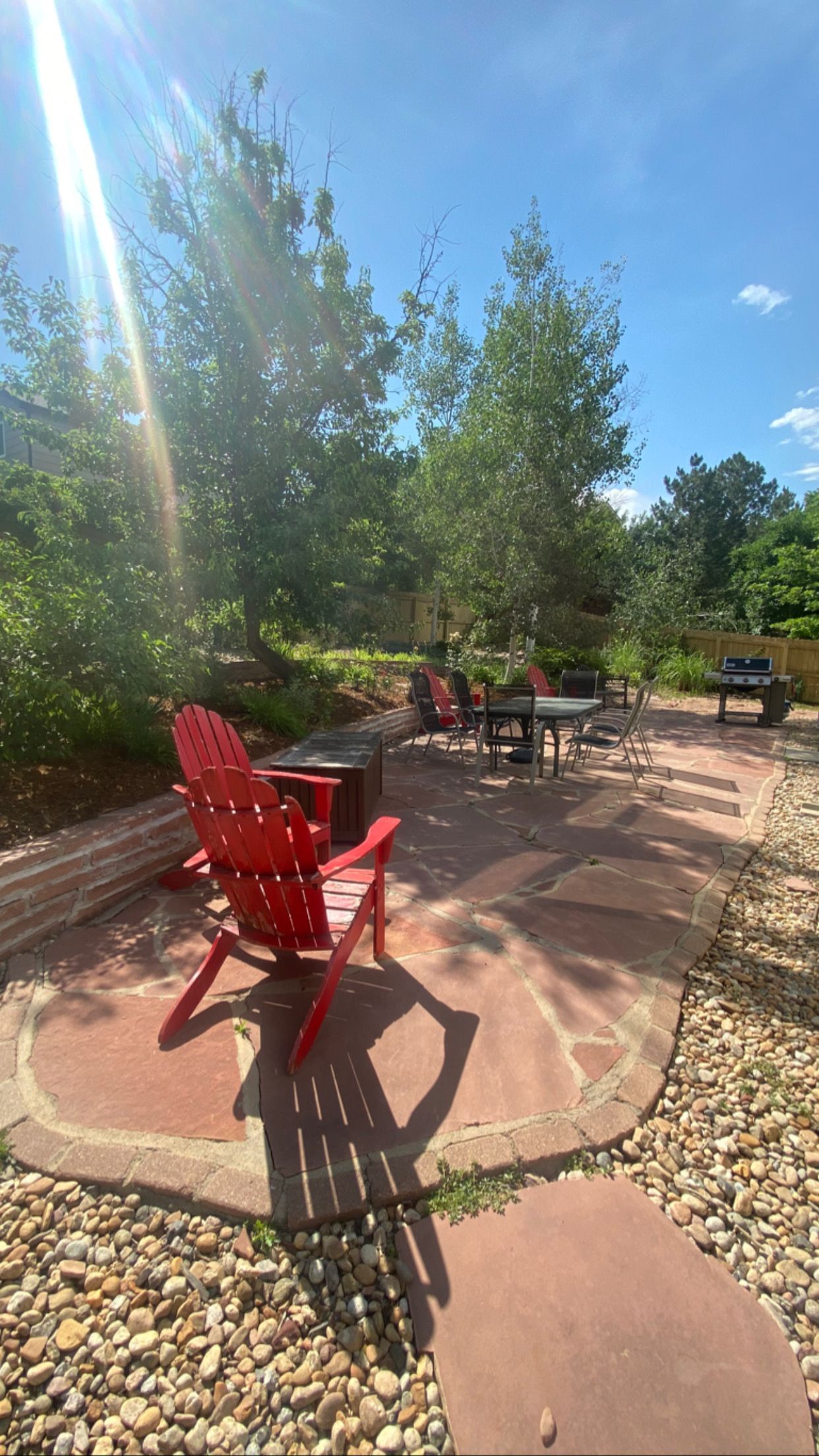 Red Adirondack chair on a patio, with trees and sunlight.