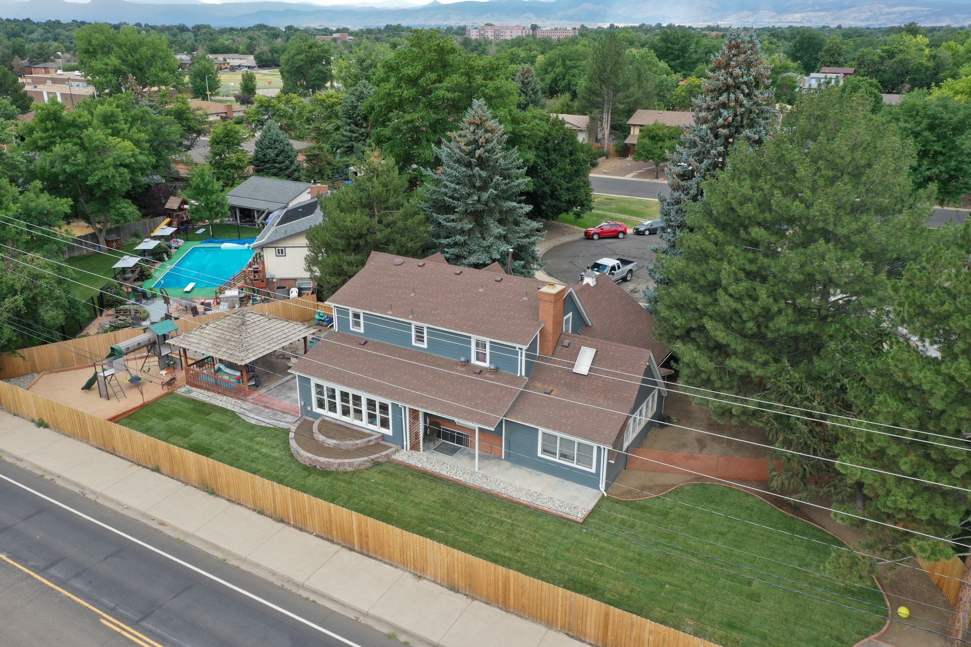 Aerial view of a blue house with a brown roof and a pool in the backyard, surrounded by trees.