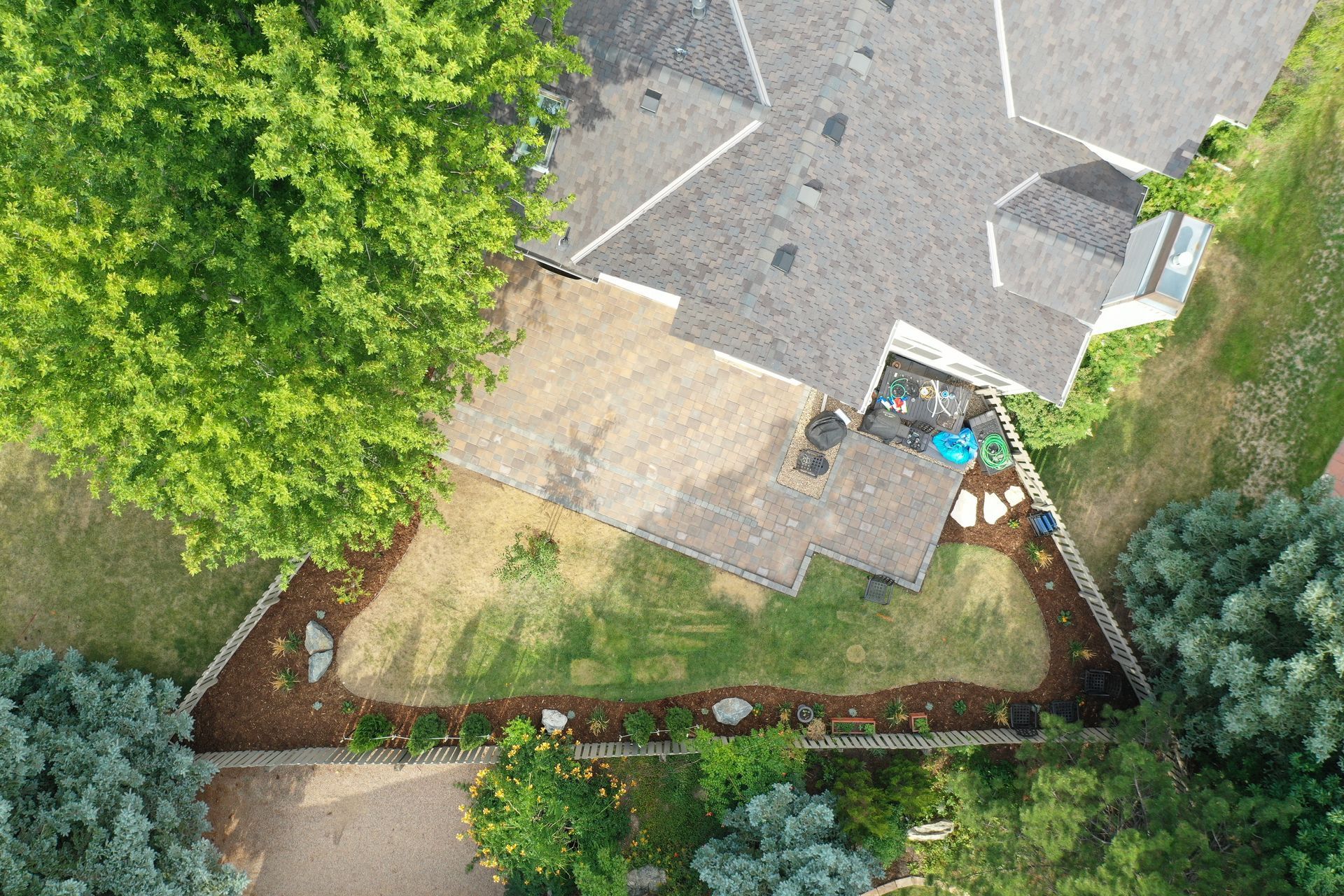 Aerial view of a house with a brown roof and a backyard with a triangular garden bed.