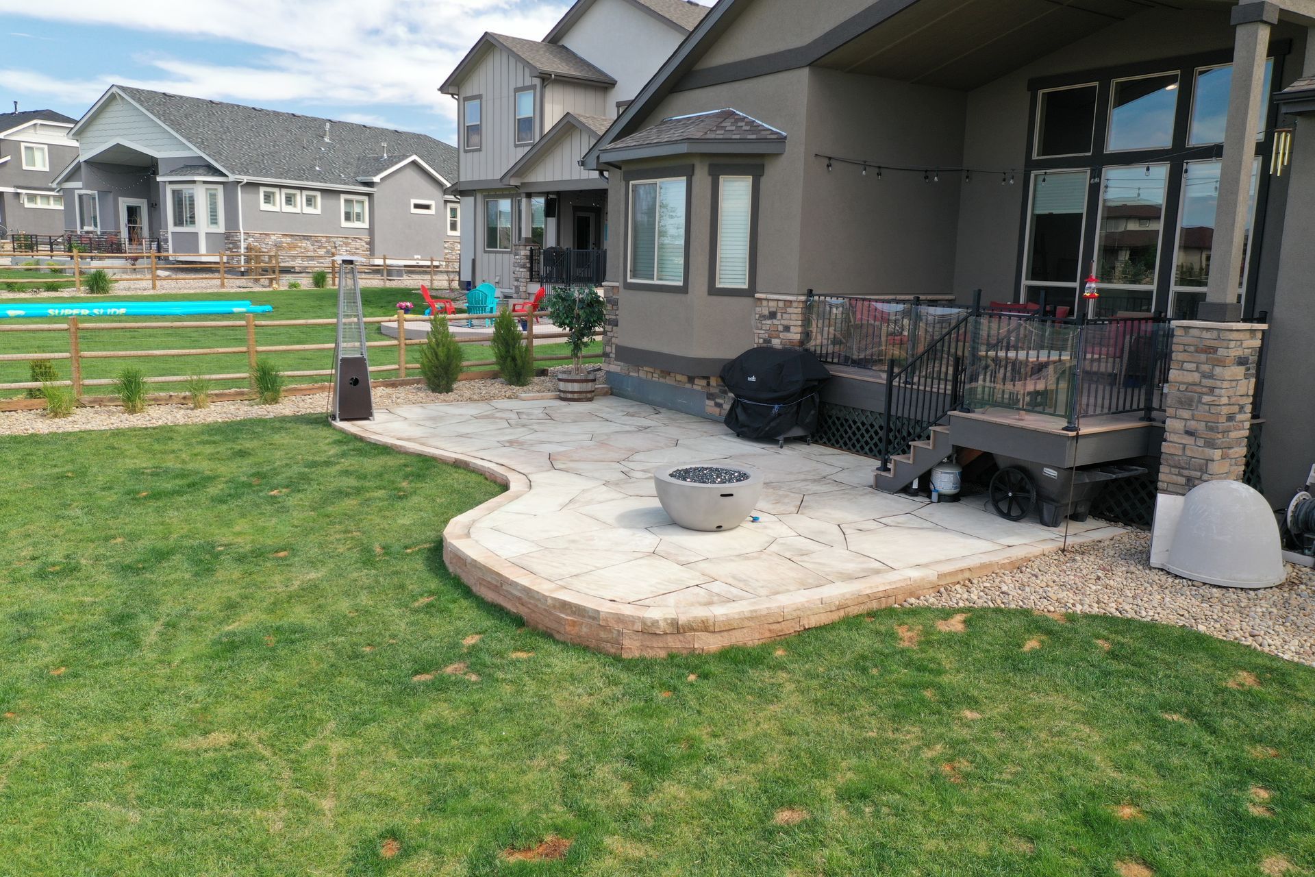 A backyard patio with a fire pit, next to a house with a green lawn.