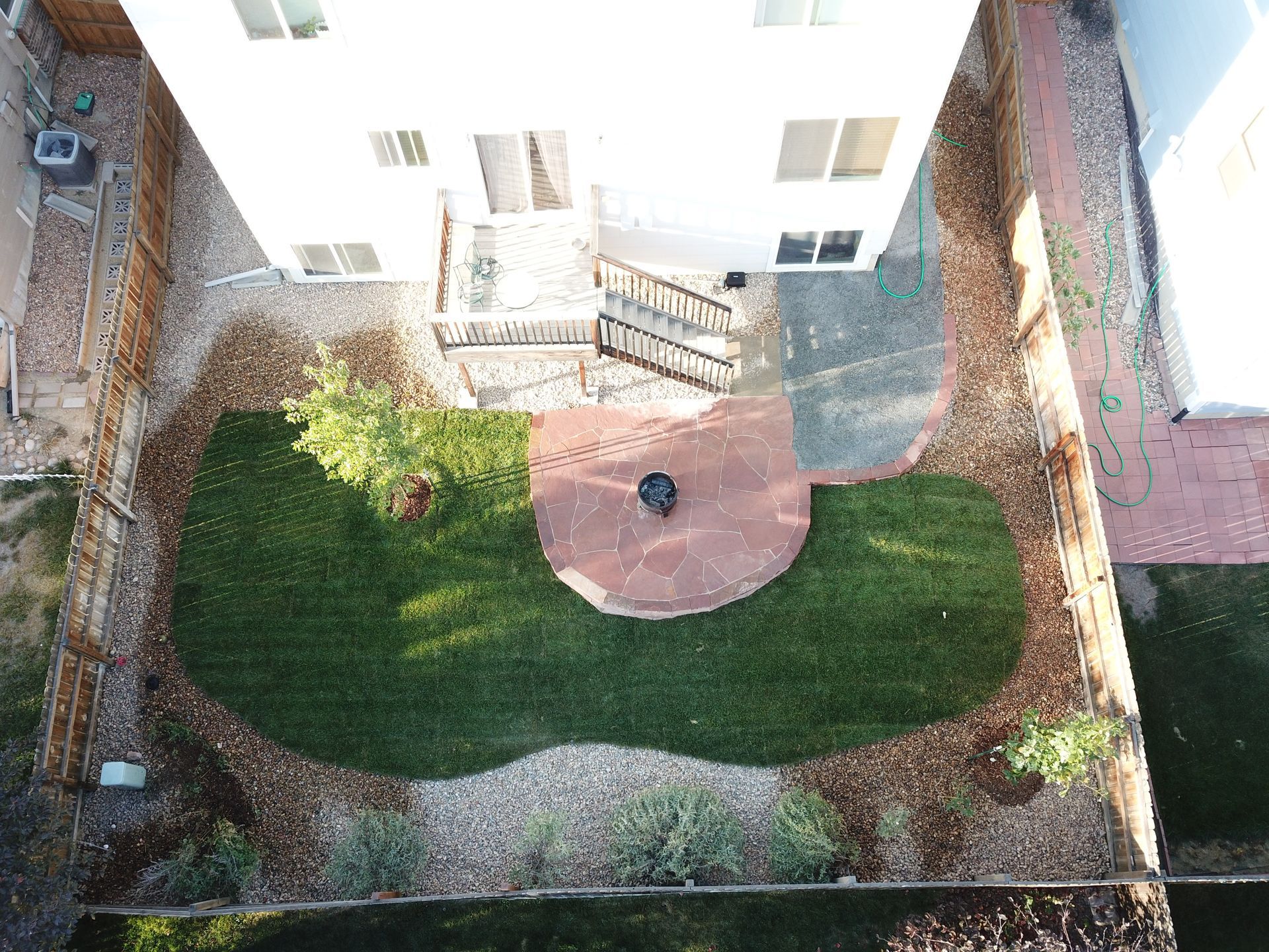 Overhead view of a backyard with a circular brick patio, a grassy area, and a white house.