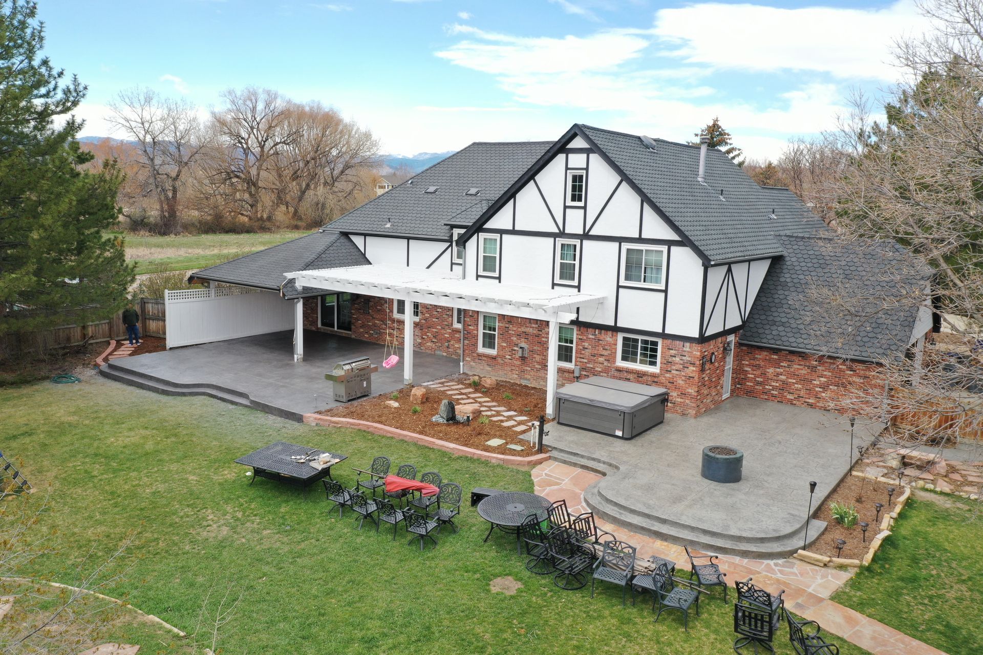 Tudor-style house with black and white exterior, patio, hot tub, and lawn.