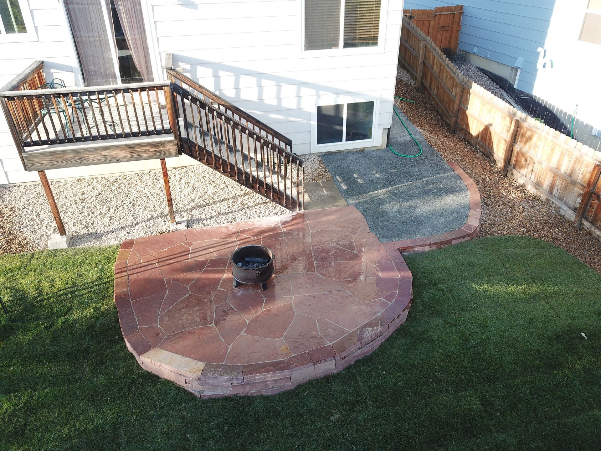 Backyard with a stone fire pit on green grass, a wooden deck, and a white house.