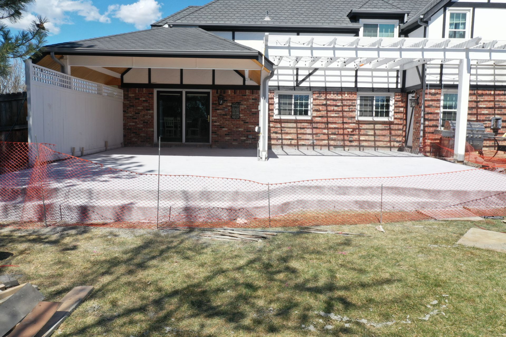 Backyard under construction with a patio, pergola, and brick wall. Orange safety fence.